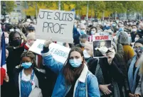  ?? ( Charles Platiau/ Reuters) ?? PEOPLE GATHER Sunday at Paris’ Republique Square to pay tribute to Samuel Paty, the French teacher who was beheaded on the streets of a Paris suburb, with a Placard reading ‘ I am a teacher.’