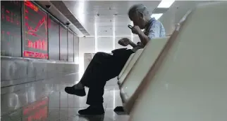  ?? NG HAN GUAN/THE ASSOCIATED PRESS ?? A Chinese stock investor uses a magnifying glass to look at his mobile phone screen as he monitors stock prices. Chinese stocks are down more than 20 per cent from their June peak.