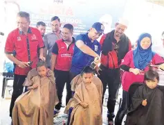  ??  ?? HAPPY: Ahmad Marzuki with Puteri UMNO cutting the hair of one of the students who took part in the Ceria Back To School Program at the Semporna Umno division office yesterday.