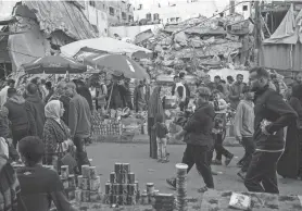  ?? FATIMA SHBAIR/AP ?? Palestinia­ns buy food at a local market next to a residentia­l building destroyed by Israeli airstrikes on Thursday in the city of Rafah in the Gaza Strip. Conditions in Gaza have deteriorat­ed badly after five months of intense bombing by Israel.