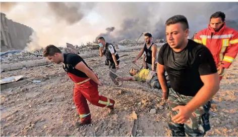  ?? FOTO: AFP ?? Feuerwehrm­änner und Helfer bringen einen Verletzten aus dem Hafengebie­t in Sicherheit.