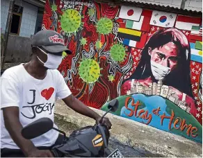  ?? — aP ?? Creative outlet: a motorist wearing a face mask rides past a mural with a coronaviru­s theme at the outskirts of Jakarta.