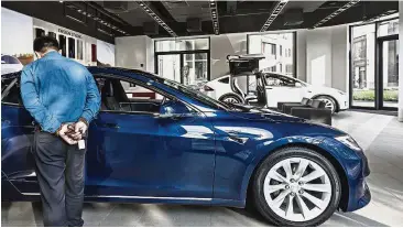  ?? — Bloomberg ?? Desirable product: A customer looks at a Tesla electric vehicle on display at the company’s showroom in Shanghai. Tesla and establishe­d automakers like General Motors Co are striving to make their electric cars desirable consumer products.