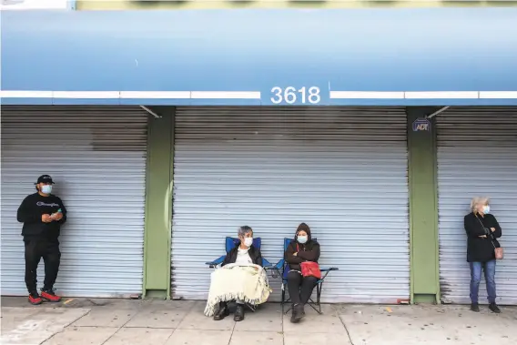  ?? Photos by Jessica Christian / The Chronicle ?? Domingo Pelayo, 83 (center), from Mexico now visiting family in Oakland, and his wife bundle up, sitting 6 feet from others waiting in line to see Ramírez.