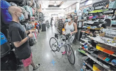  ?? Wilfredo Lee The Associated Press ?? Guillermo Ley, left, an employee at Fritz’s Skate Bike & Surf store in Miami Beach, Fla., helps Michelle Deleon on Wednesday. Miami, Miami Gardens, Hialeah and Miami Beach began phased openings of some shops Wednesday.