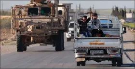  ?? HUSSEIN MALLA / AP ?? Syrian boys, right, sit in a pickup truck and flash victory signs as they pass by a U.S. military vehicle March 31 in Manbij, north Syria.