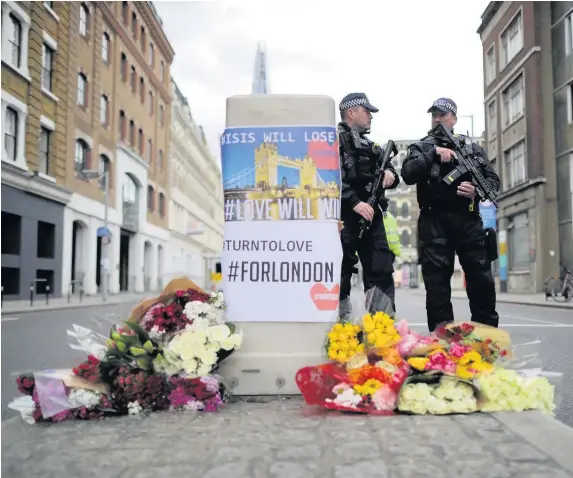  ??  ?? > Armed police stand guard in front of floral tributes on Southwark Street near the scene of Saturday night’s terrorist attack in London