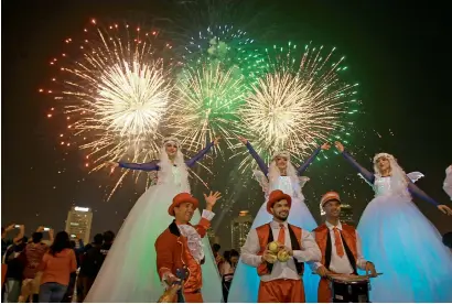  ?? Photo by Shihab ?? Stilt walkers and performers with the DSF’s opening fireworks in the background at Al Seef, Dubai, on Tuesday. —