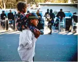  ?? RAMON ESPINOSA ASSOCIATED PRESS ?? A migrant carries a child past Mexican police outside Benito Juarez Sports Center, which is serving as a shelter for migrants, in Tijuana, Mexico, on Monday.