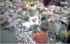  ?? EMILIO MORENATTI/THE ASSOCIATED PRESS ?? A child places flowers in a square in central Manchester, Britain.