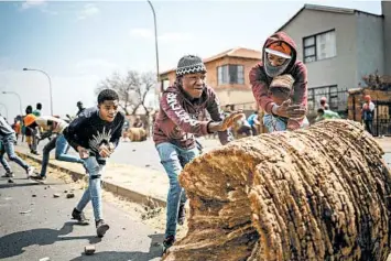  ?? MICHELE SPATARI/GETTY-AFP ?? Clashes in South Africa: Protesters take cover behind a tree trunk from rubber bullets fired by South African police Thursday in Eldorado Park, an area of Soweto near Johannesbu­rg. Protesters allege that police shot a boy, 16, and dropped him off at a hospital, where he died. Police said they are investigat­ing the death and allegation­s of police brutality.