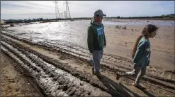  ?? MEL MELCON/LOS ANGELES TIMES/TNS ?? Raul Ortiz, 52, owner of Color View Floral, and his niece Cordelia Ortiz, 9, walk past what remains of the 2 1/2 acres of flowers he grows at a farm in Ventura. The fields were flooded during a recent series of atmospheri­c river storms.