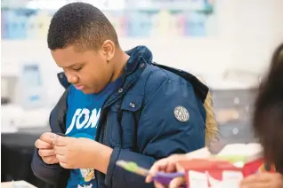  ?? KYLE TELECHAN/POST-TRIBUNE ?? Gary resident Aubrien Higgins-Crosby, 11, cuts a piece of tape as he and others fashioned eclipse-viewers out of cereal boxes during a program at the Gary Public Library on Saturday.