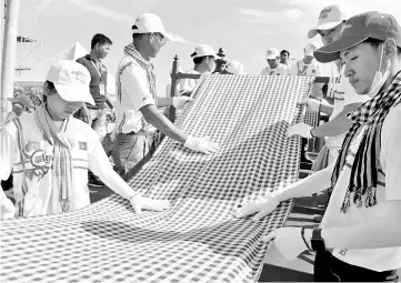  ?? — AFP photo ?? Cambodians roll out a 1,149.8 metre-long krama scarf so it can be declared as the world’s longest hand woven scarf, in Phnom Penh.