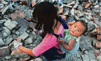  ?? Reuters ?? A migrant worker collects bricks as she carries her child on her back at a demolition site in Jiaxing, Zhejiang province, China.