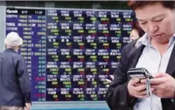  ??  ?? TOKYO: A man uses a mobile phone in front of an electronic stock indicator of a securities firm in Tokyo, yesterday. —AP