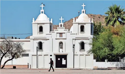  ??  ?? Un hombre pasa por fuera de la iglesia Nuestra Señora de Guadalupe, en Guadalupe, Arizona