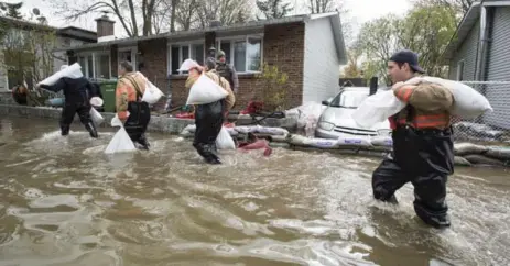  ?? PAUL CHIASSON/THE CANADIAN PRESS ?? Firemen carry sandbags to protect a house on Île Bizard, in the southweste­rn part of Montreal, Tuesday.