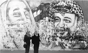  ??  ?? Palestinia­n students stand in front of a mural depicting the late Hamas leader Ahmed Yassin and the late Palestinia­n leader Yasser Arafat, in Gaza City. — Reuters photo