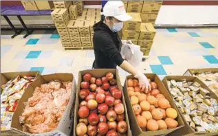  ?? Irfan Khan Los Angeles Times ?? A LOS ANGELES UNIFIED SCHOOL DISTRICT cafeteria worker prepares food bags at James A. Garfield High School for distributi­on among local families earlier in the COVID-19 pandemic.