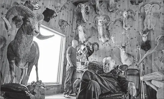  ?? [LEAH NASH/THE NEW YORK TIMES] ?? Vance Corrigan, considered to be one of the most accomplish­ed big-game hunters, sits in his trophy room at his home in Livingston, Montana. With him is Brendan Burns, a former Ohio State wrestler who is a sheep hunter and guide in Montana. Wealthy...