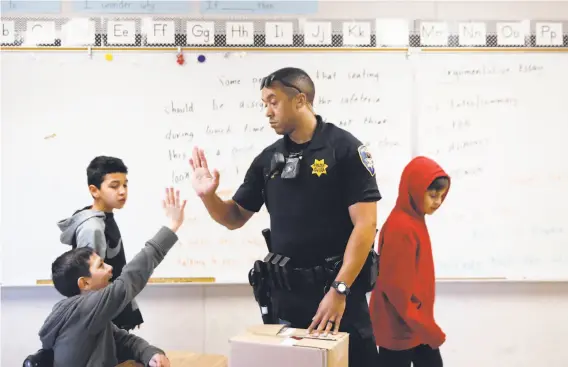  ?? Michael Macor / The Chronicle ?? Hayward police Officer Julian Cosgriff gives a high-five to Juan Pablo Gamino before the gang-resistance session at Bowman Elementary School.