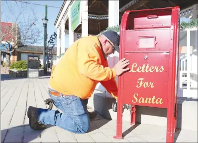  ?? (NWA Democrat-Gazette/David Gottschalk) ?? Josh Murr, with the city of Huntsville Public Works, places the last bolt to brace a dedicated mailbox for Santa Claus at Polk Square in downtown Huntsville. The square is decorated with a holiday light display including a new Christmas Tree.