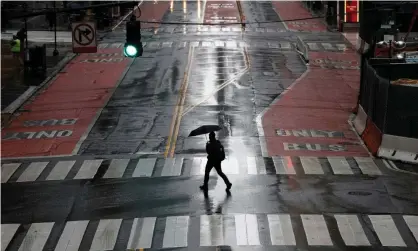  ??  ?? A man carries an umbrella as he walks across an empty East 42nd Street in New York, New York. In the city, Latinx residents make up 34% of coronaviru­s deaths. Photograph: Mike Segar/Reuters