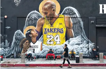  ?? AP Photo/Damian Dovarganes ?? ■ People lift weights on a sidewalk Monday outside the Hardcore Fitness gym, due to COVID-19 restrictio­ns, under a mural honoring NBA star Kobe Bryant and his daughter Gigi near Staples Center in downtown Los Angeles. Bryant, who became one of the greatest basketball players of his generation during a 20-year career with the Lakers, died in a helicopter crash with his daughter Gigi and other passengers on Jan. 26, 2020.