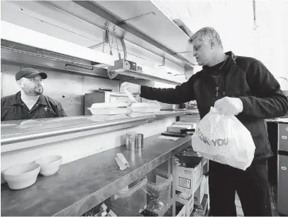  ?? ELAINE THOMPSON AP ?? Glen Quadros, owner of the Great American Diner & Bar, checks a takeout order as cook Arturo Aguilar looks on in Seattle.