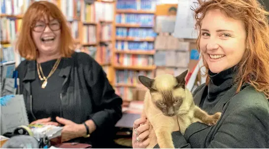  ?? BEVAN READ/FAIRFAX NZ ?? Time Out owner Wendy Tighe-Umbers, left, and Claire Duncan share a laugh with the store’s ‘‘brat of a cat’’, which does not appear to be in on the joke.