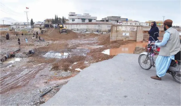  ?? Agence France-presse ?? Onlookers gaze towards municipal workers using heavy machinery to level the ground after damage due to floodwater­s on the outskirts of Quetta on Monday.