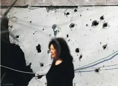  ?? ARIEL SCHALIT / THE ASSOCIATED PRESS ?? A woman walks by a house hit by a rocket fired from the Gaza Strip, in the Israeli city of Ashkelon Tuesday.