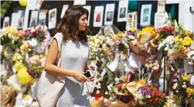  ?? (AFP) ?? This file photo shows a woman walking past flowers, left as a tribute to the victims and the missing from the Grenfell Tower block fire outside Notting Hill Methodist Church, in west London on June 19