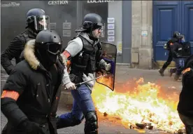  ?? ASSOCIATED PRESS ?? Riot police run past burning dustbins set on fire by yellow vest protesters as they keep pressure on French President Emmanuel Macron’s government with the 13th straight weekend of demonstrat­ions in Paris.