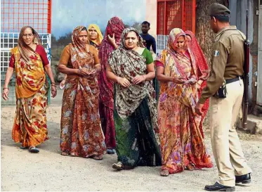  ??  ?? Security check: A policeman checking the identity papers of several women as they arrive to cast their votes at a polling station in Panshina village of Surendrana­gar district. — Reuters