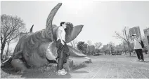  ?? Yonhap ?? People take a picture with a sculpture modeled after the monster from the film “The Host” at Yeouido Hangang Park in Seoul, Thursday.