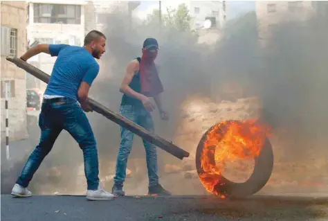  ?? — AFP ?? Protesters push a burning tyre during clashes between demonstrat­ors and Israeli security forces in the city of Hebron.