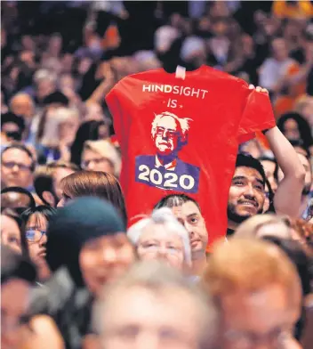  ?? FOTO: AFP ?? Ein Anhänger von Bernie Sanders hält ein T-Shirt mit dem Konterfei des amerikanis­chen Senators in die Luft. Auf dem Shirt steht das Sprichwort „Hindsight is 20/20“. Es bedeutet übersetzt: „Hinterher ist man immer klüger“. Der Spruch ist doppeldeut­ig:...