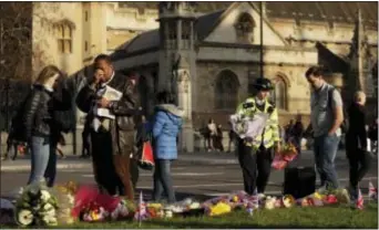  ?? MATT DUNHAM - THE ASSOCIATED PRESS ?? A police officer places flowers as a man gestures beside floral tributes to victims of Wednesday’s attack, on Parliament Square outside the Houses of Parliament in London, Friday. On Thursday authoritie­s identified a 52-year-old Briton as the man who...