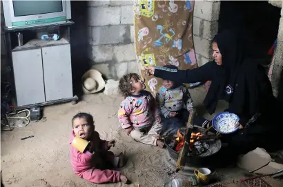  ?? — Reuters ?? A Palestinia­n woman feeds her daughter as they sit by a fire on a rainy day in Khan Younis in the southern Gaza Strip on Friday.