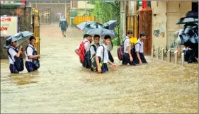  ?? IANS ?? Students walk on flooded streets in Mumbai on Friday.