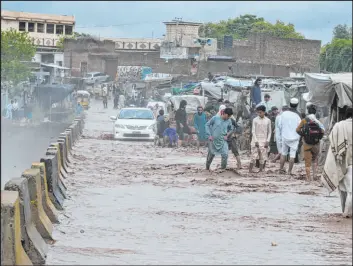  ?? Muhammad Sajjad The Associated Press ?? People wade Monday through a flooded bridge on a stream, which is overflowin­g following deadly heavy rains, on the outskirts of Peshawar, Pakistan.