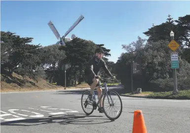  ?? Photos by Lea Suzuki / The Chronicle ?? Bicyclists ride along on a “slow street” on MLK Drive past the Murphy Windmill in Golden Gate Park.