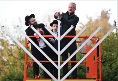  ?? PHOTOS BY CHRIS RILEY — THE REPORTER ?? Vacaville mayor John Carli lights the shammash on the Vacaville menorah with Rabbi Chaim Zaklos and his son Mendel during the first night of Chanukah on Thursday.