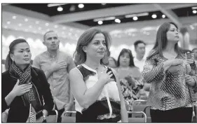  ?? The New York Times/JENNA SCHOENEFEL­D ?? Mona Wattar (center) and Alma Dominguez (right) stand for the national anthem during a naturaliza­tion ceremony Oct. 17 in Los Angeles.