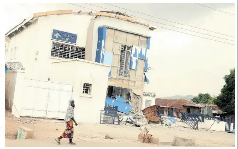  ??  ?? A woman walks by damaged government offices in Michika, a town Nigeria’s military has recaptured from Boko Haram.