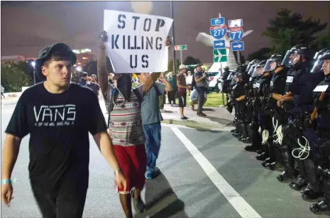  ??  ?? Protesters walk past riot police blocking off a ramp to a highway during a demonstrat­ion against police brutality in Charlotte, North Carolina, on Thursday following the shooting of Keith Lamont Scott two days earlier and two nights of riots. Hundreds...