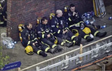  ?? MATT DUNHAM — THE ASSOCIATED PRESS ?? Firefighte­rs rest as they take a break in battling a massive fire that raged in a high-rise apartment building in London, Wednesday. Fire swept through a high-rise apartment building in west London early Wednesday, killing an unknown number of people...