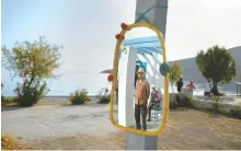  ?? AP-Yonhap ?? Hotel owner Akis Sartzetaki­s and his friend are reflected in a mirror as three men jog past next to the beach on the Aegean Sea island of Tilos, southeaste­rn Greece, Tuesday.